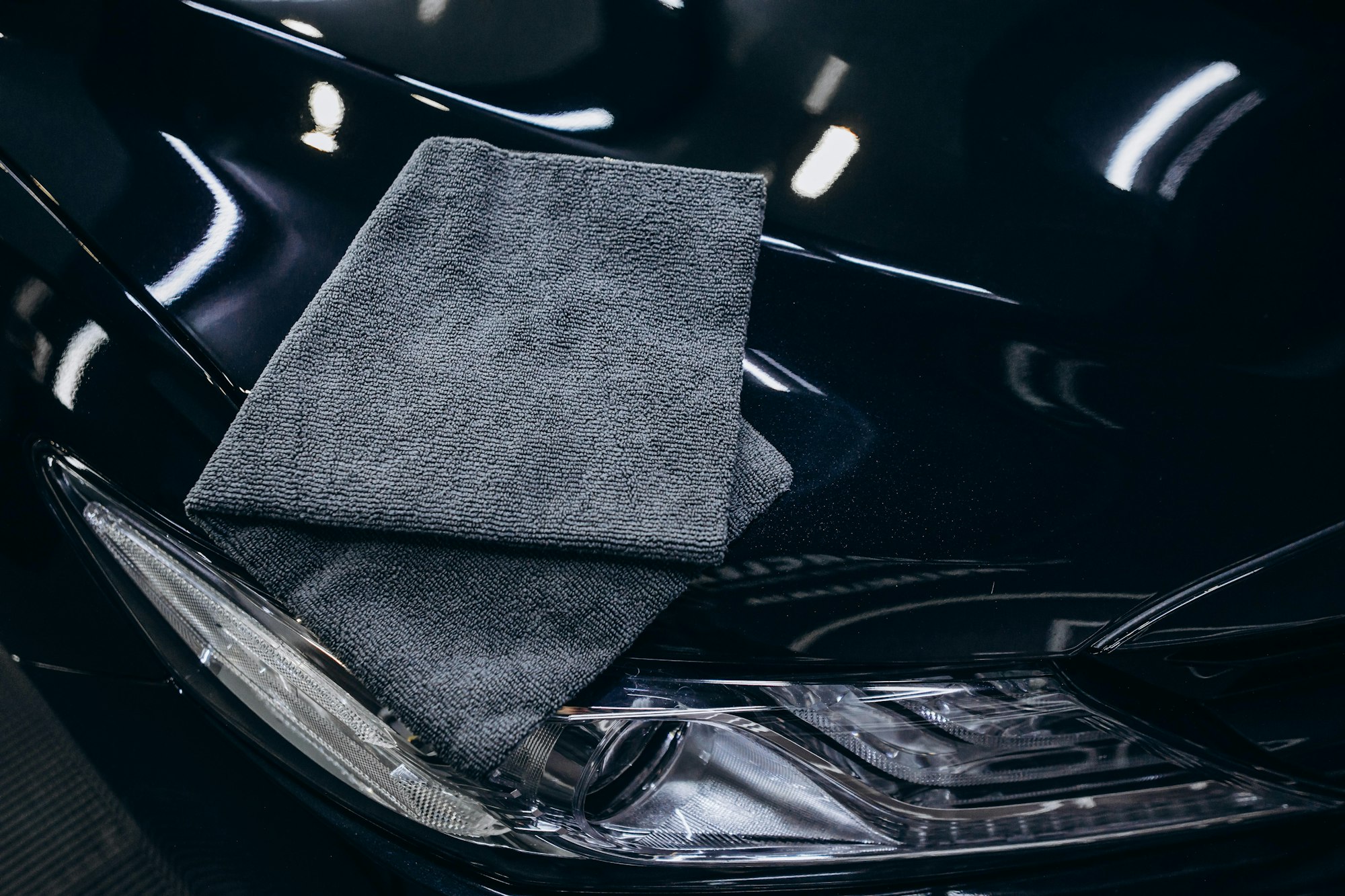 Microfiber cloth resting on a glossy black car hood beside a headlight