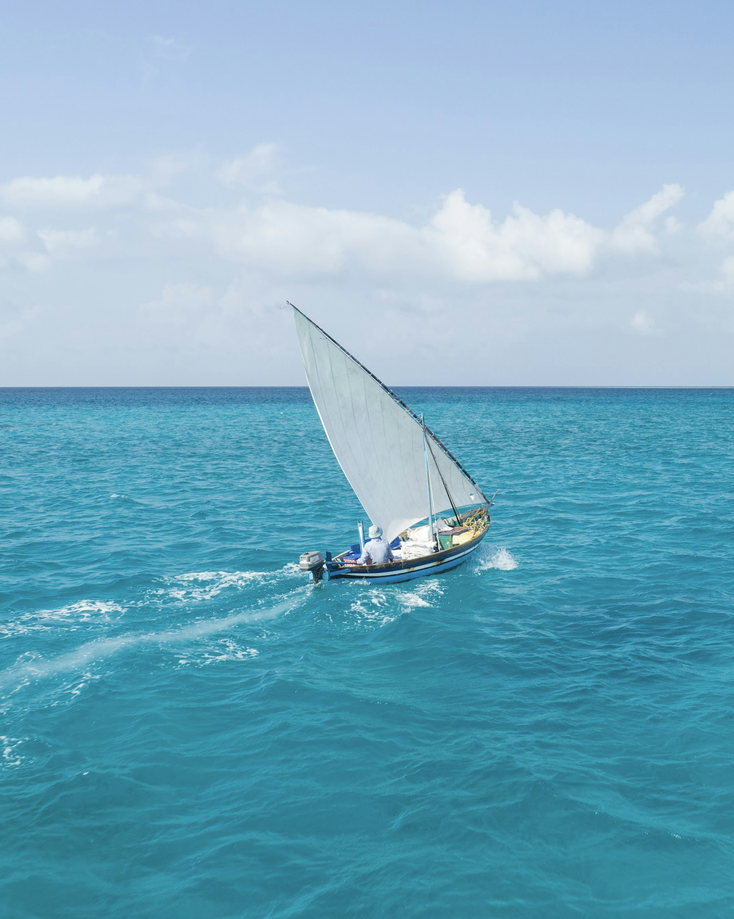 Small white sailboat underway on open turquoise water